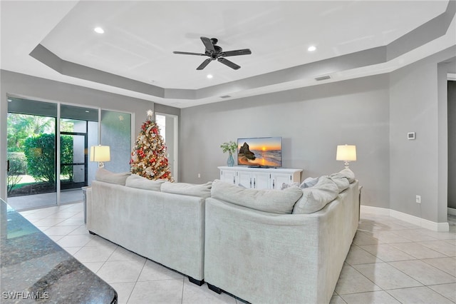 tiled living room with a raised ceiling and ceiling fan