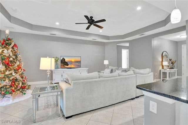 tiled living room with ceiling fan and a tray ceiling