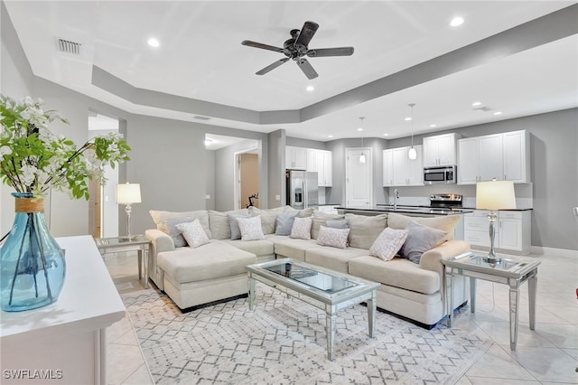 living room featuring ceiling fan, light tile patterned flooring, a raised ceiling, and sink