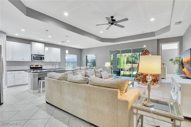 living room featuring light tile patterned floors, a raised ceiling, ceiling fan, and sink