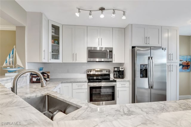 kitchen featuring backsplash, appliances with stainless steel finishes, glass insert cabinets, a sink, and light stone countertops