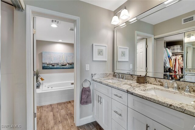 bathroom with wood-type flooring, vanity, and tiled bath