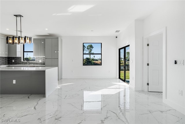 kitchen with tasteful backsplash, gray cabinetry, hanging light fixtures, and a healthy amount of sunlight