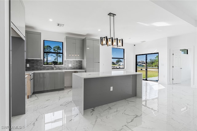 kitchen featuring gray cabinetry, backsplash, a chandelier, pendant lighting, and a kitchen island