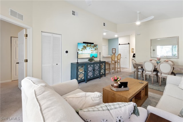 carpeted living room featuring a barn door, ceiling fan, and a high ceiling