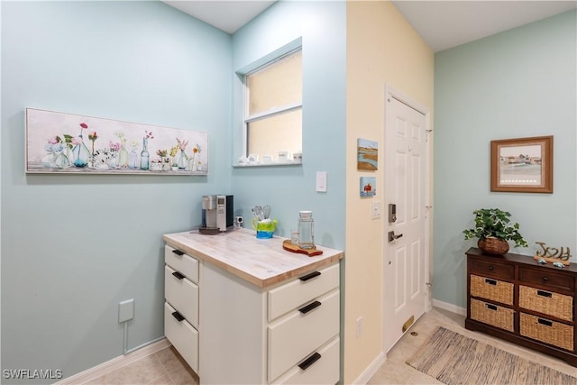 interior space with butcher block countertops, light tile patterned floors, and white cabinets