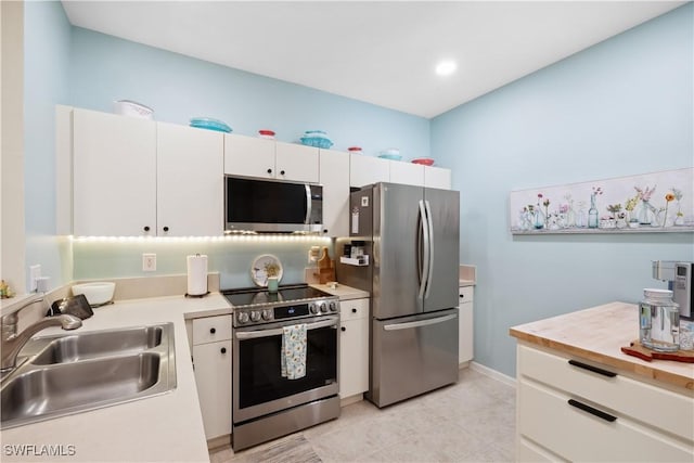 kitchen featuring butcher block counters, sink, light tile patterned floors, appliances with stainless steel finishes, and white cabinets