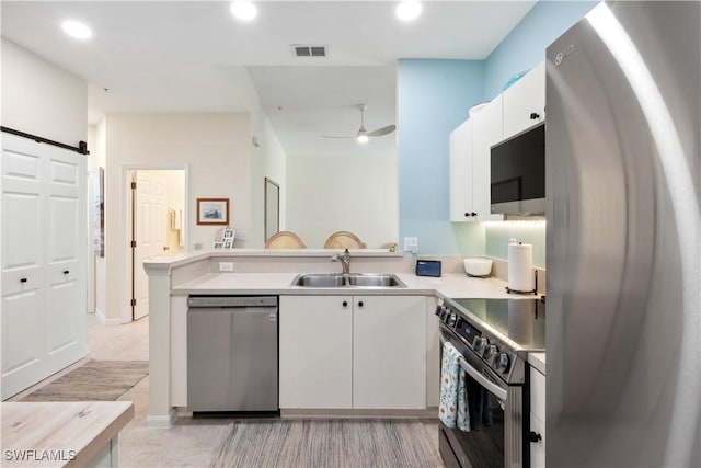 kitchen featuring appliances with stainless steel finishes, white cabinetry, sink, kitchen peninsula, and a barn door