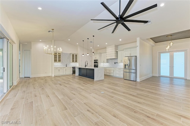 kitchen featuring hanging light fixtures, stainless steel fridge, a center island with sink, white cabinets, and light wood-type flooring