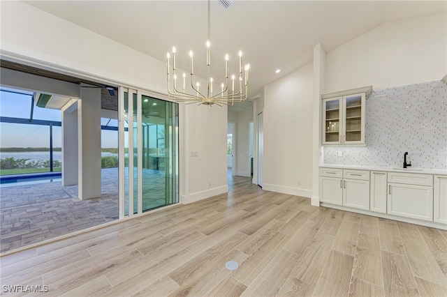 unfurnished dining area with vaulted ceiling, light wood-type flooring, sink, and an inviting chandelier