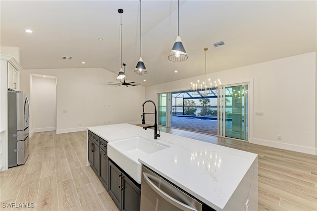 kitchen with light stone countertops, sink, lofted ceiling, a center island with sink, and appliances with stainless steel finishes