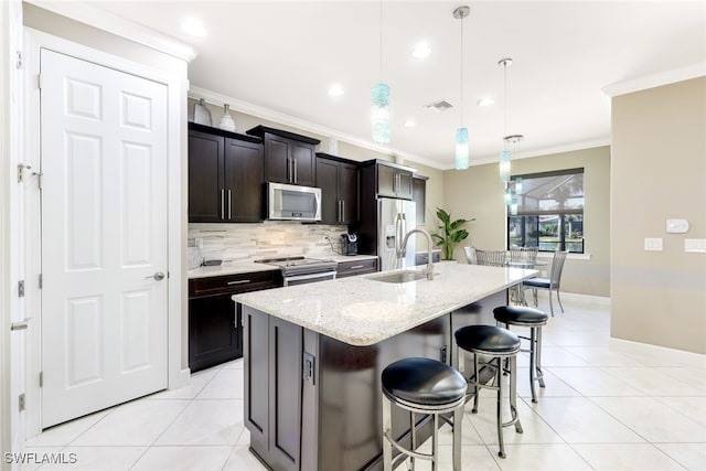 kitchen with ornamental molding, stainless steel appliances, sink, pendant lighting, and a center island with sink