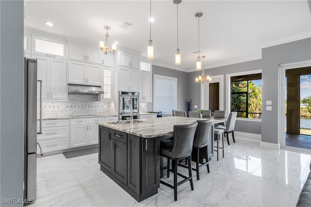 kitchen featuring light stone counters, stainless steel appliances, white cabinetry, hanging light fixtures, and an island with sink