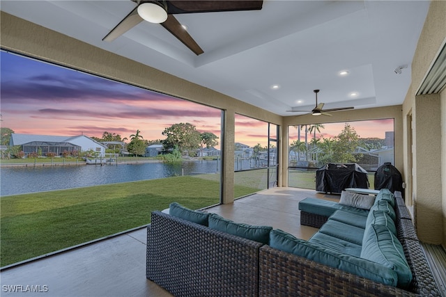 sunroom featuring a tray ceiling, ceiling fan, and a water view