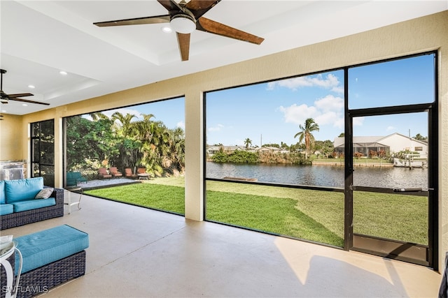 unfurnished sunroom with a tray ceiling, ceiling fan, a water view, and a healthy amount of sunlight