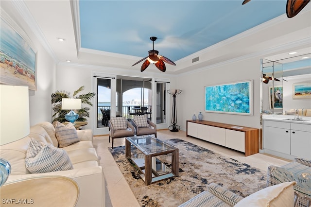 tiled living room featuring a raised ceiling, ceiling fan, sink, and ornamental molding