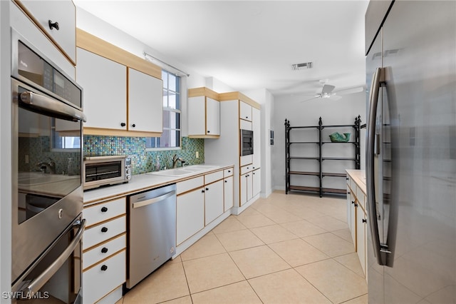 kitchen featuring ceiling fan, sink, backsplash, white cabinets, and appliances with stainless steel finishes