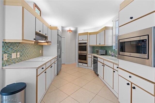 kitchen with sink, light tile patterned flooring, backsplash, built in appliances, and white cabinets