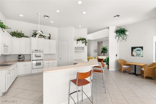 kitchen featuring white cabinetry, a breakfast bar, an island with sink, and white appliances