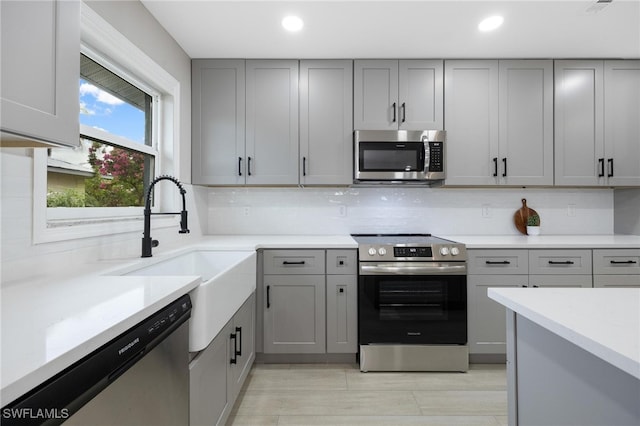 kitchen with appliances with stainless steel finishes, tasteful backsplash, gray cabinetry, and sink