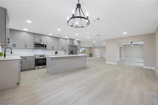 kitchen with gray cabinetry, stainless steel appliances, ceiling fan with notable chandelier, and light wood-type flooring