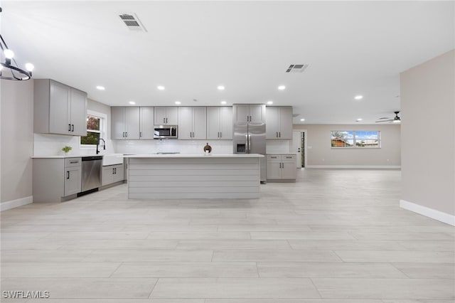 kitchen featuring gray cabinetry, a center island, sink, stainless steel appliances, and ceiling fan with notable chandelier