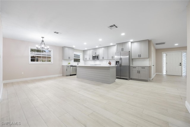 kitchen featuring stainless steel appliances, decorative light fixtures, gray cabinets, a kitchen island, and light wood-type flooring