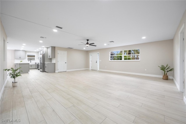 unfurnished living room with ceiling fan, sink, and light hardwood / wood-style floors