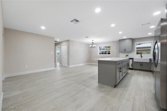 kitchen featuring gray cabinetry, sink, a kitchen island, and light wood-type flooring