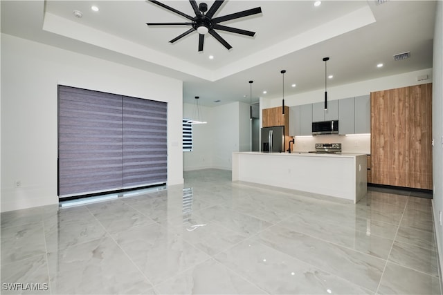 kitchen with a center island, stainless steel appliances, a raised ceiling, and hanging light fixtures