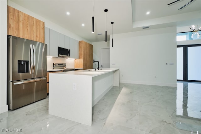 kitchen with white cabinets, decorative light fixtures, a center island with sink, and stainless steel appliances