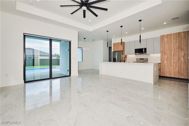 kitchen with decorative light fixtures, ceiling fan, stainless steel appliances, and a tray ceiling