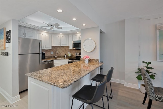 kitchen featuring white cabinets, ceiling fan, appliances with stainless steel finishes, a kitchen bar, and kitchen peninsula