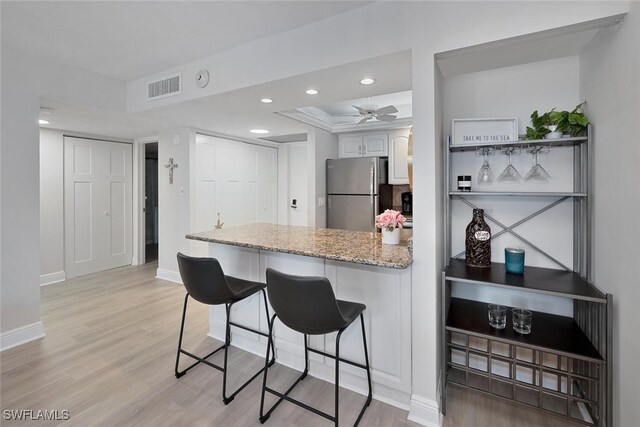 kitchen featuring ceiling fan, light stone counters, stainless steel fridge, light hardwood / wood-style floors, and a breakfast bar area