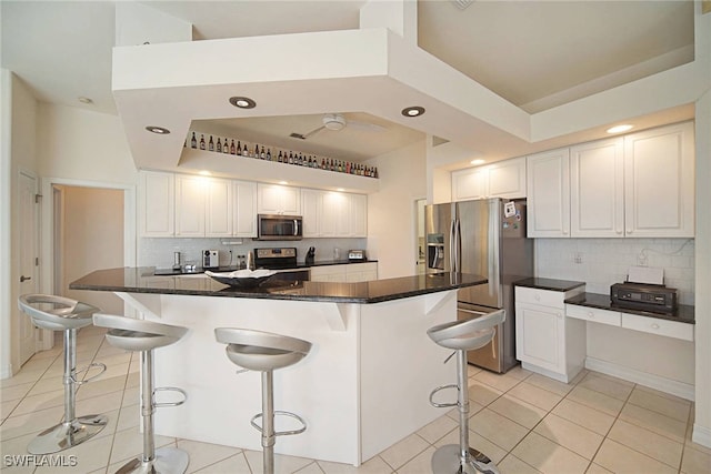 kitchen with light tile patterned floors, a kitchen island, a kitchen bar, white cabinetry, and stainless steel appliances