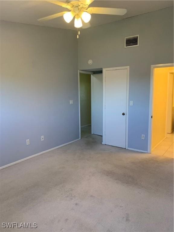 unfurnished bedroom featuring a high ceiling, a closet, light colored carpet, and ceiling fan