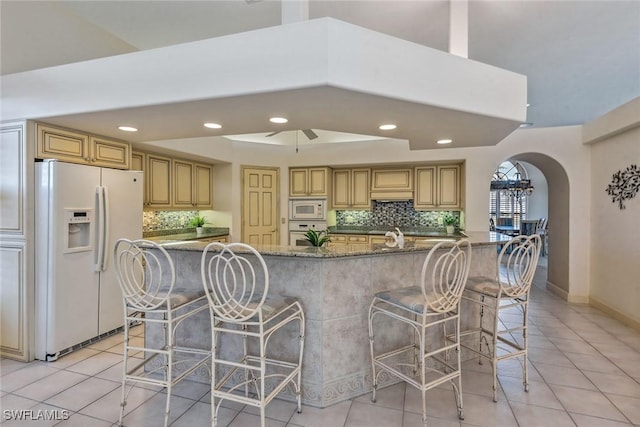 kitchen featuring white appliances, dark stone countertops, a breakfast bar, and a large island with sink