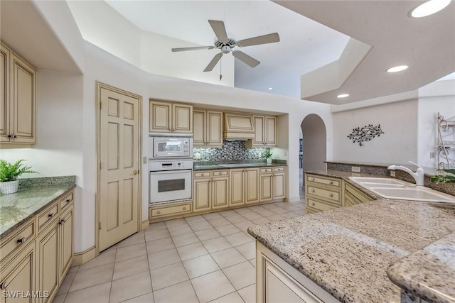 kitchen with white appliances, light tile patterned floors, arched walkways, decorative backsplash, and a sink