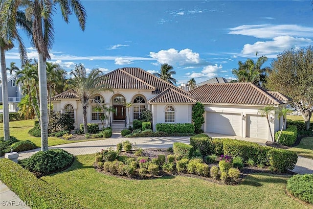 mediterranean / spanish-style house featuring a garage, a front lawn, a tile roof, and stucco siding