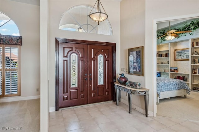 entrance foyer featuring light carpet, ceiling fan, a towering ceiling, and baseboards