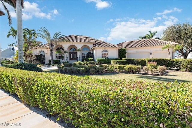 mediterranean / spanish home with a tiled roof, stucco siding, an attached garage, and a front yard