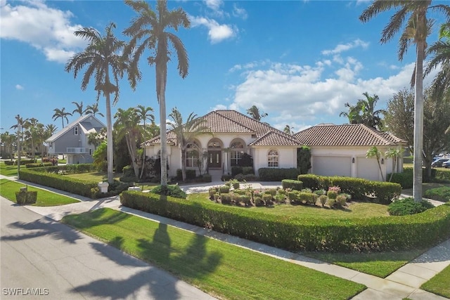 mediterranean / spanish house with an attached garage, stucco siding, a tiled roof, and a front yard