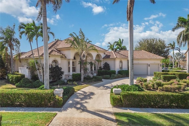 mediterranean / spanish home with a garage, a tile roof, decorative driveway, and stucco siding