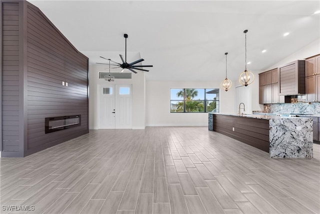 kitchen featuring pendant lighting, backsplash, light stone countertops, ceiling fan with notable chandelier, and vaulted ceiling