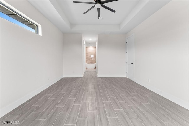 unfurnished living room featuring a raised ceiling, ceiling fan, and light hardwood / wood-style flooring