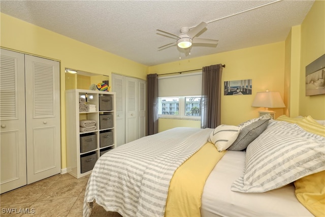 bedroom with ceiling fan, light tile patterned floors, a textured ceiling, and multiple closets