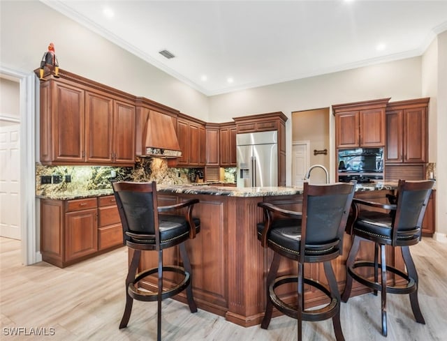 kitchen featuring light stone counters, custom exhaust hood, stainless steel built in fridge, light wood finished floors, and tasteful backsplash