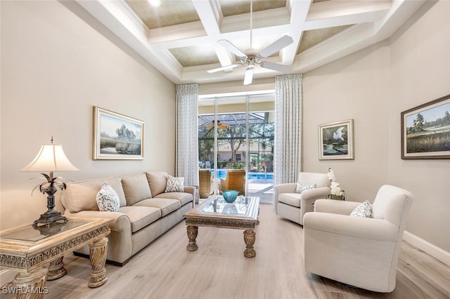 living area featuring a towering ceiling, a ceiling fan, a sunroom, wood finished floors, and baseboards