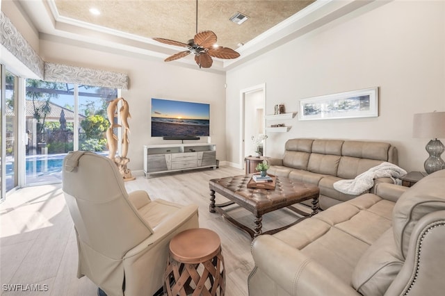 living room with light wood-type flooring, visible vents, a tray ceiling, and baseboards