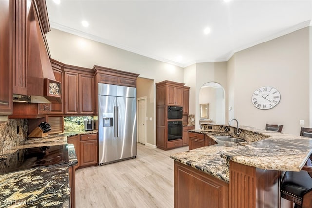 kitchen with light stone counters, a sink, stainless steel built in refrigerator, black oven, and range